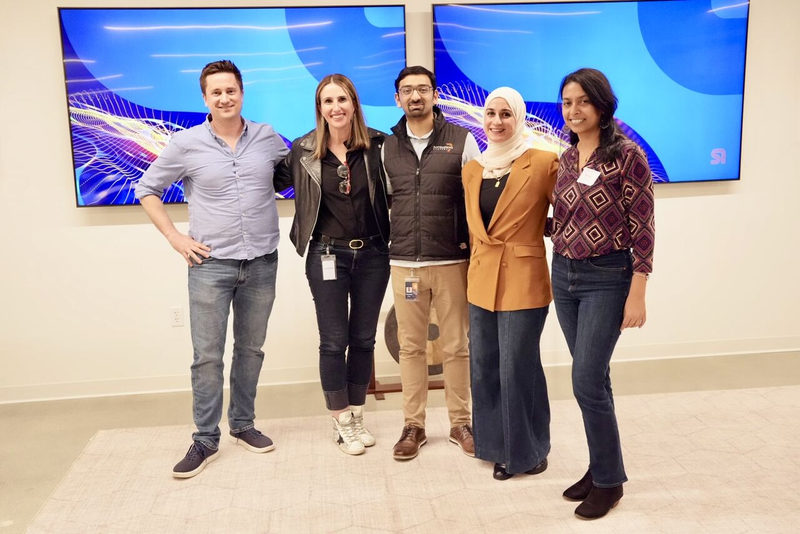 Five attendees posing together in front of blue event screens.